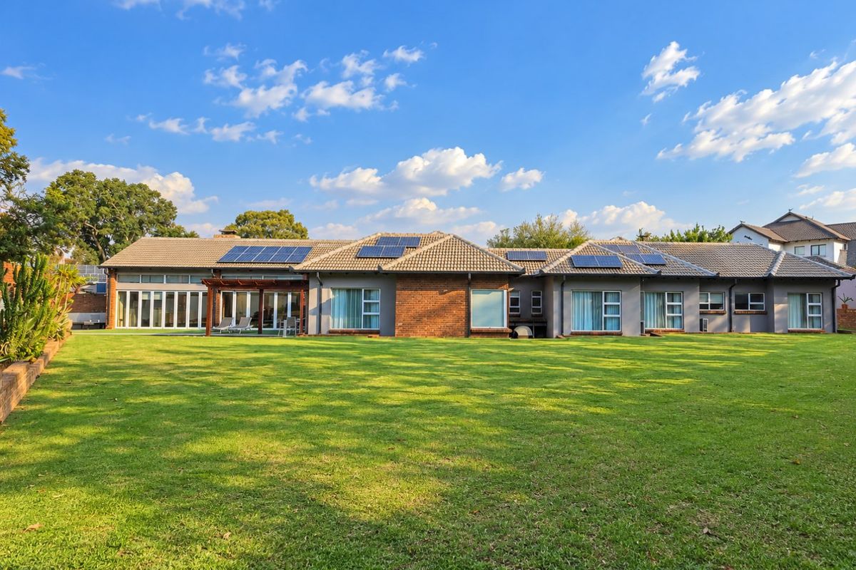 Spacious rear exterior view of a well-maintained house featuring a large lawn, solar panels, and a covered patio area with sliding glass doors.