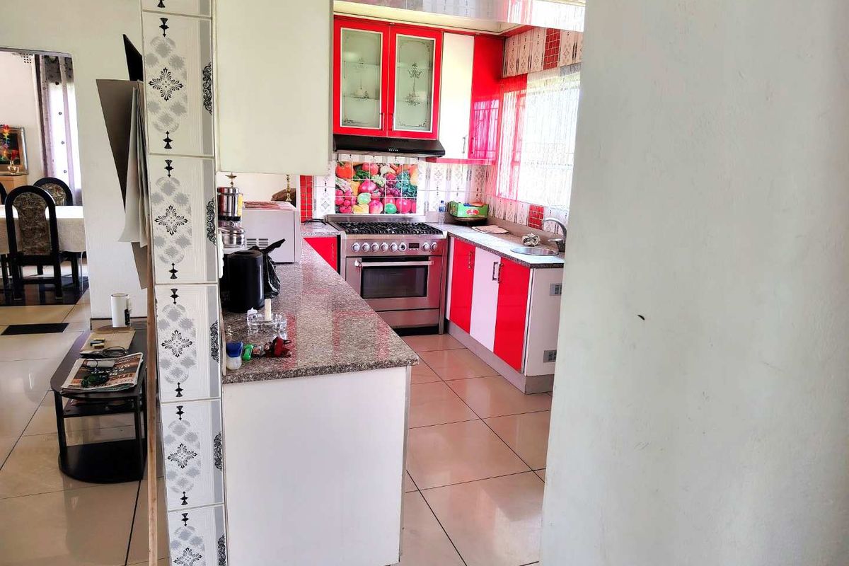 A functional kitchen featuring red and white cabinetry, granite countertops, a built-in gas stove with extractor fan, and tiled flooring throughout.