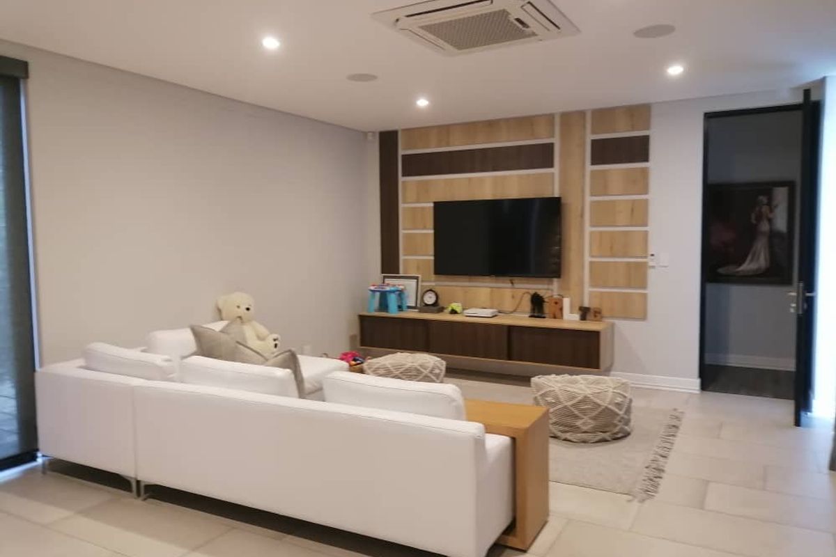 Modern living room featuring a custom wood-paneled media wall, recessed ceiling lighting, integrated air conditioning unit, and neutral tiled flooring.