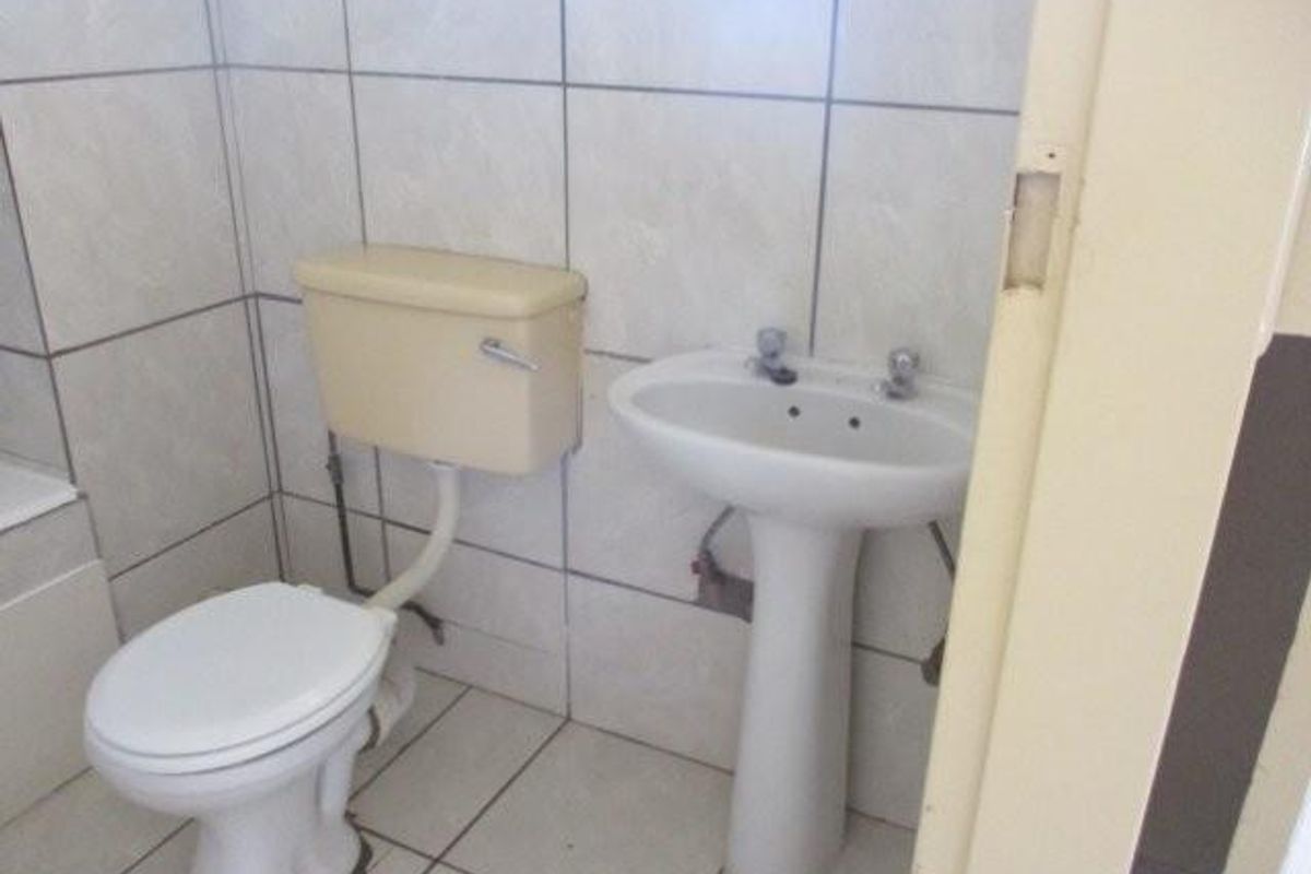 A functional bathroom featuring a pedestal basin and toilet with neutral ceramic wall and floor tiling, presenting an opportunity for modernization.
