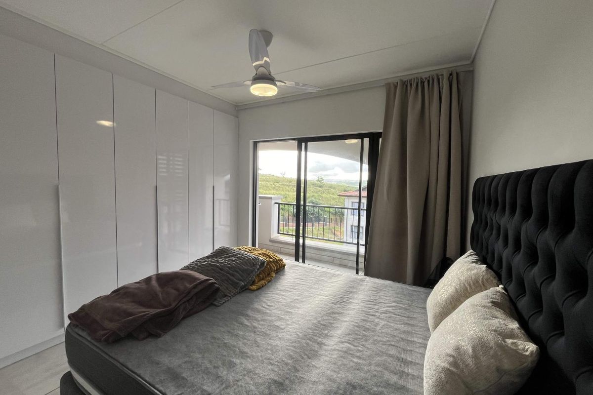 A well-maintained bedroom featuring floor-to-ceiling built-in cupboards, a modern ceiling fan, and sliding glass doors leading to a private balcony with scenic views.