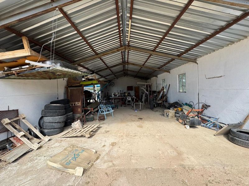 A spacious, functional farm garage or workshop featuring a high corrugated metal roof, exposed steel trusses, and a durable concrete floor.