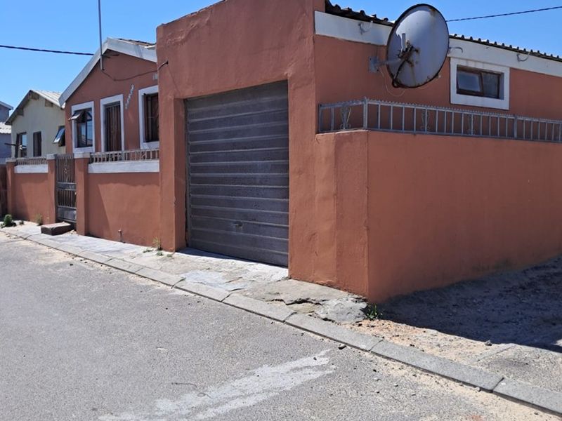 Street-facing view of a residential property featuring a roller garage door, boundary wall with security fencing, and exterior wall finishes.