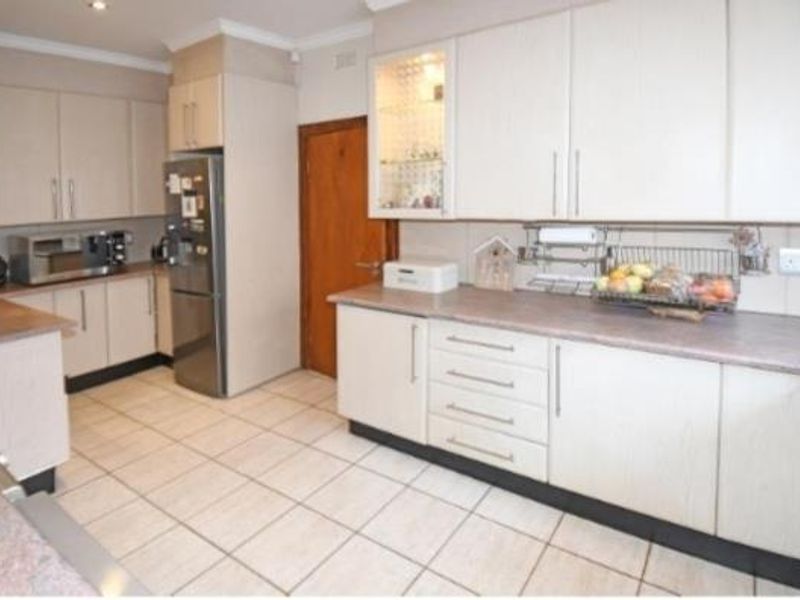 A functional kitchen featuring light-toned laminate cabinetry, ample countertop workspace, and tiled flooring, offering a clean and practical layout for daily use.