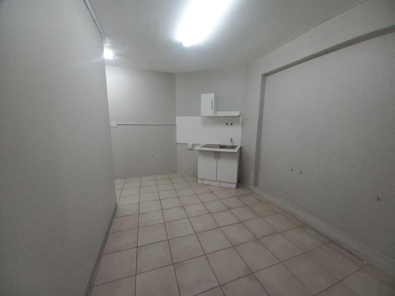 A compact, empty kitchen area featuring tiled flooring, basic cabinetry, and a single sink unit, suitable for a small office or utility space.