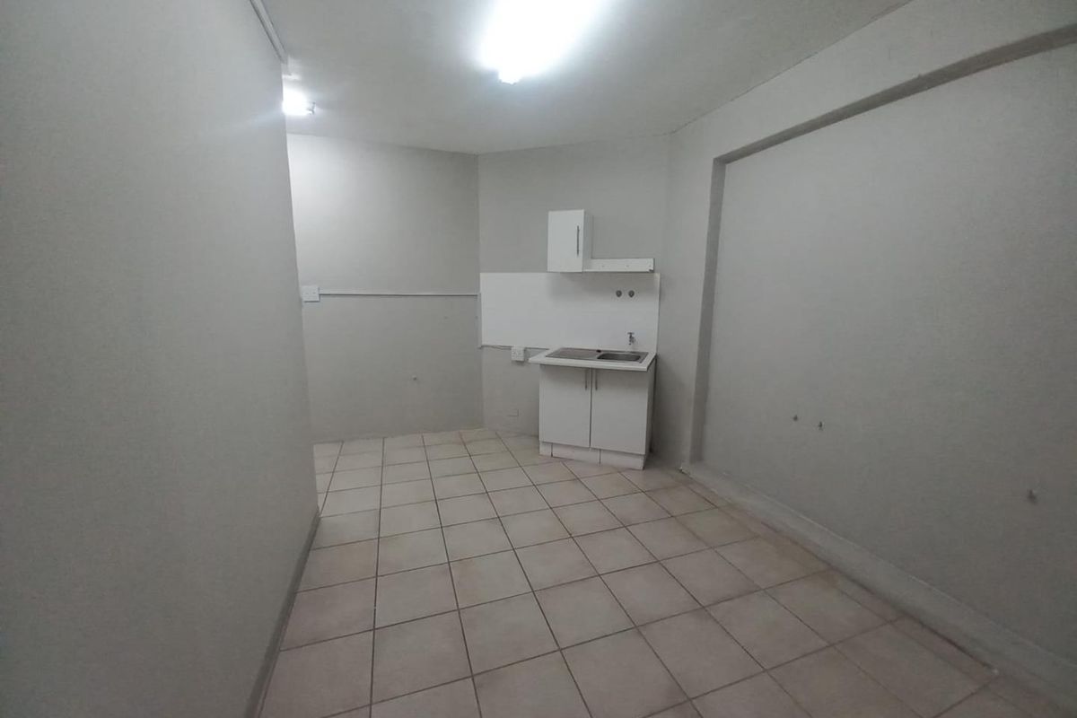 A compact, empty kitchen area featuring tiled flooring, basic cabinetry, and a single sink unit, suitable for a small office or utility space.
