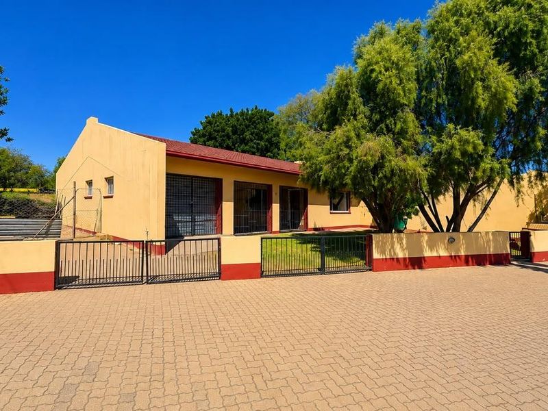 Front exterior view of a townhouse featuring a paved driveway, perimeter wall with metal gates, and security bars on windows.