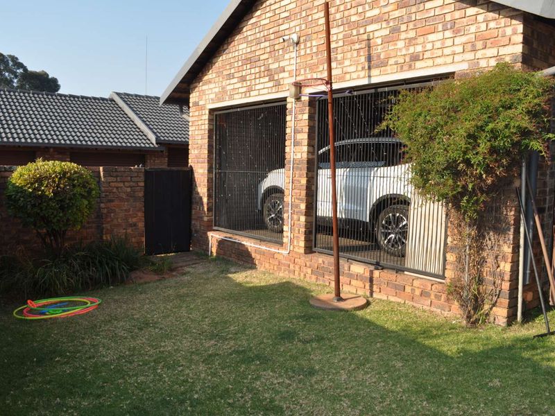 Rear view of the townhouse featuring a face brick exterior, a small lawn area, and a secure gated parking space.