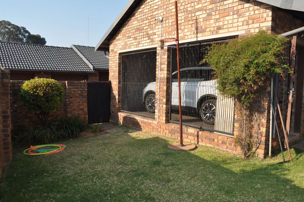 Rear view of the townhouse featuring a face brick exterior, a small lawn area, and a secure gated parking space.