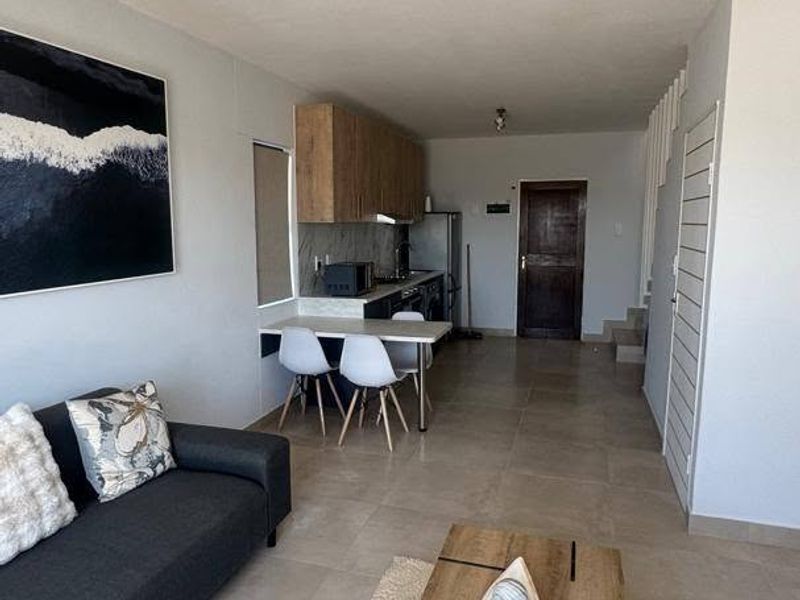 Open-plan living and kitchen area featuring neutral tiled flooring, modern cabinetry, and a staircase leading to the upper level.