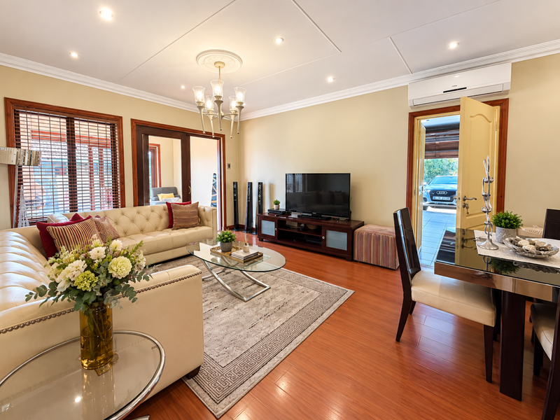 A well-maintained living room featuring laminate flooring, recessed lighting, a decorative ceiling rose with chandelier, and direct access to the exterior via sliding doors.
