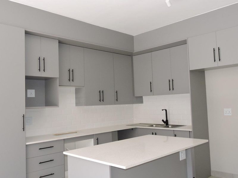 Modern kitchen featuring sleek grey cabinetry, quartz countertops, a subway tile backsplash, and a functional central island with a black mixer tap.