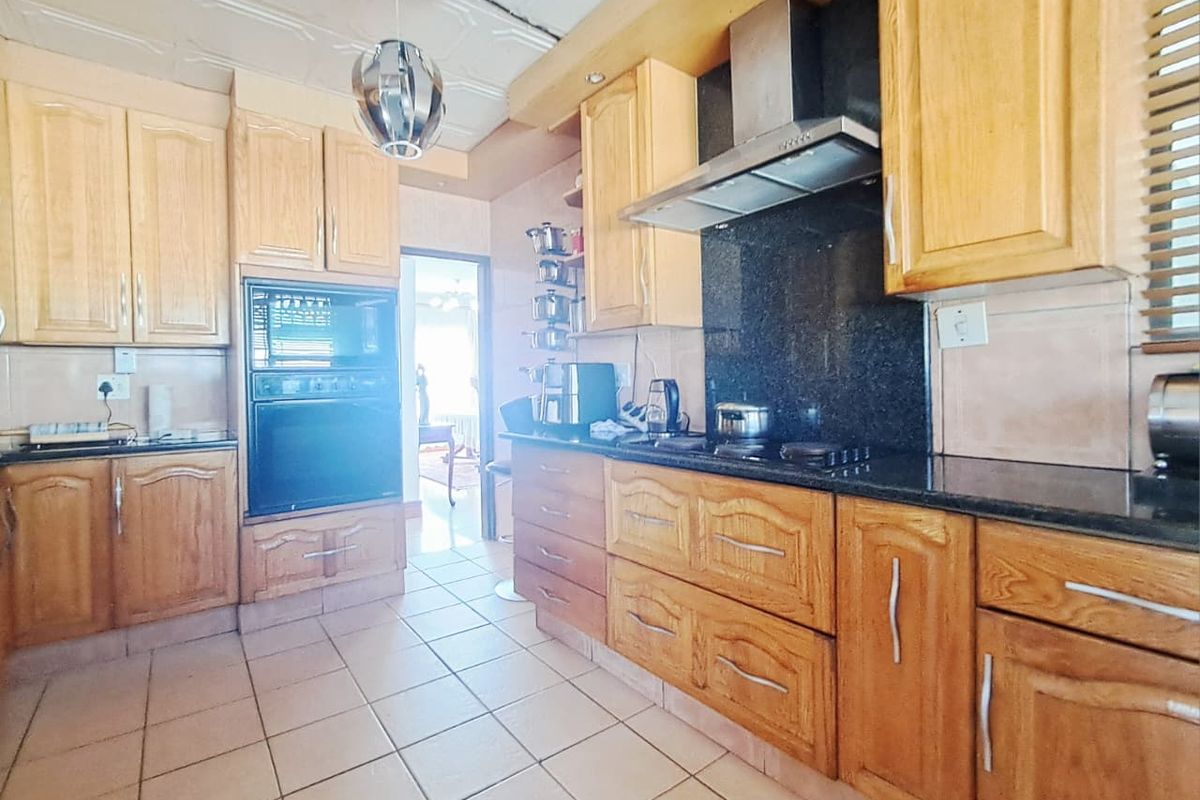 A functional kitchen featuring wooden cabinetry, granite countertops, built-in oven, and extractor fan, with tiled flooring and a decorative ceiling.