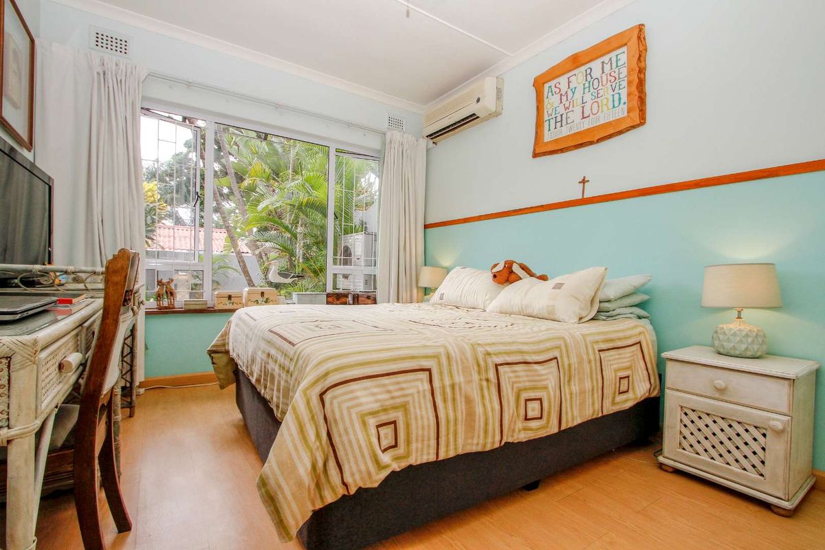 A bedroom featuring laminate flooring, large windows with security bars, and a wall-mounted air conditioning unit.