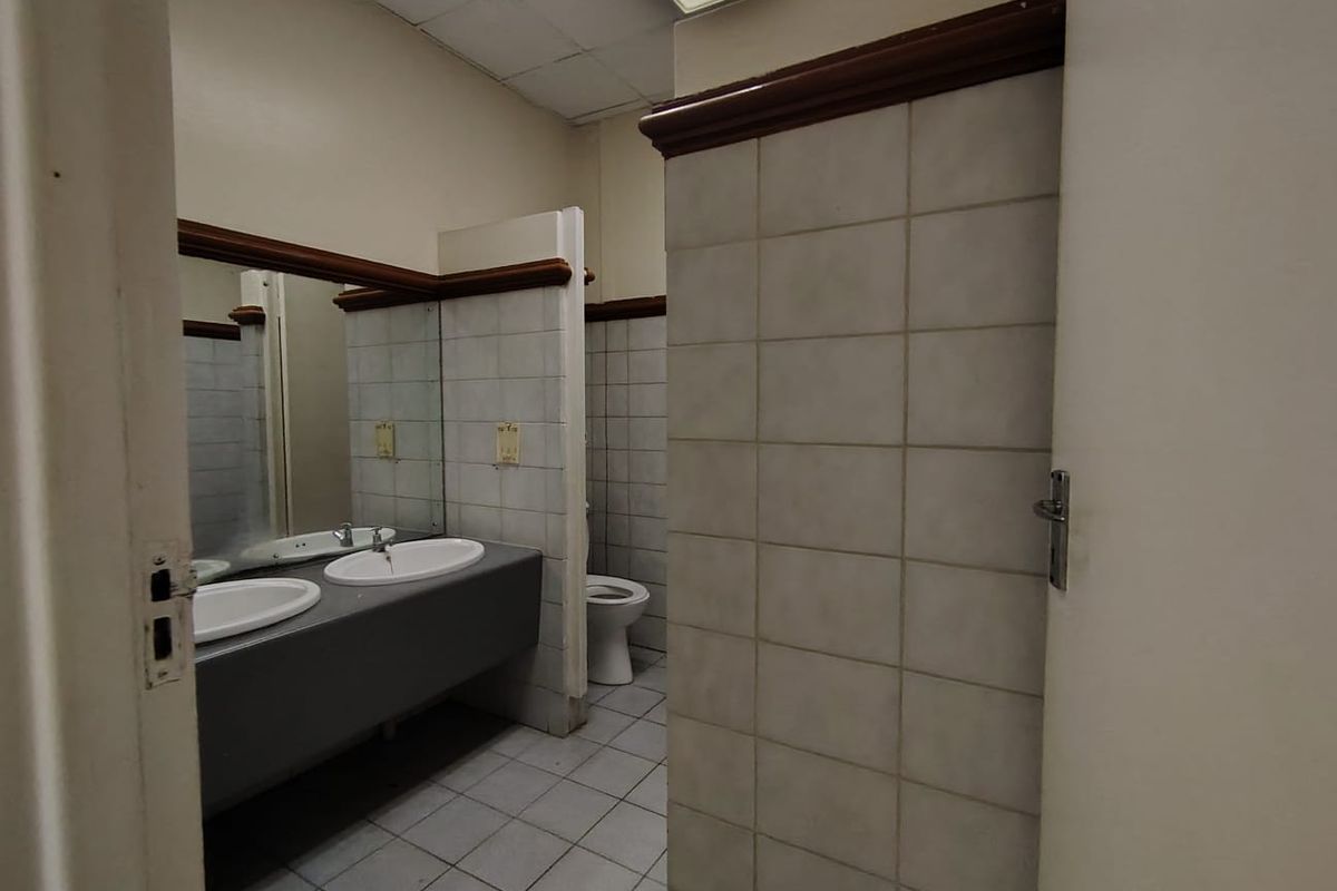 A functional commercial bathroom featuring dual vanity basins, tiled walls and flooring, and a separate toilet cubicle.