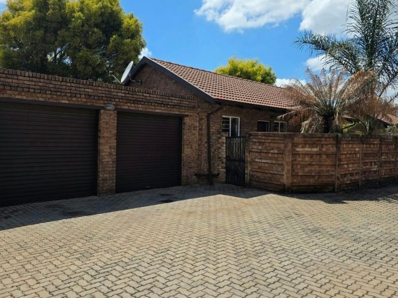 Front exterior view of a facebrick townhouse featuring a double garage, paved driveway, and secure boundary walling.