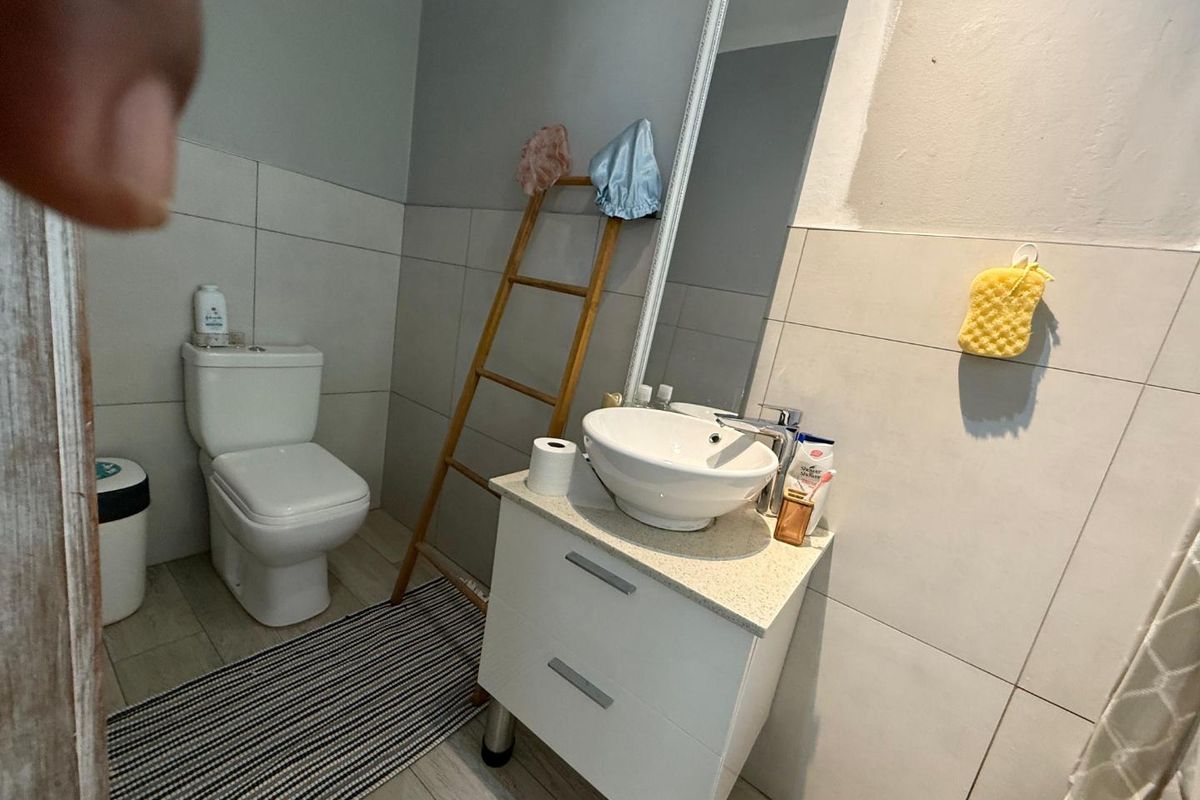 A functional bathroom featuring a modern vessel sink vanity, wall-mounted mirror, and standard toilet with neutral wall tiling.