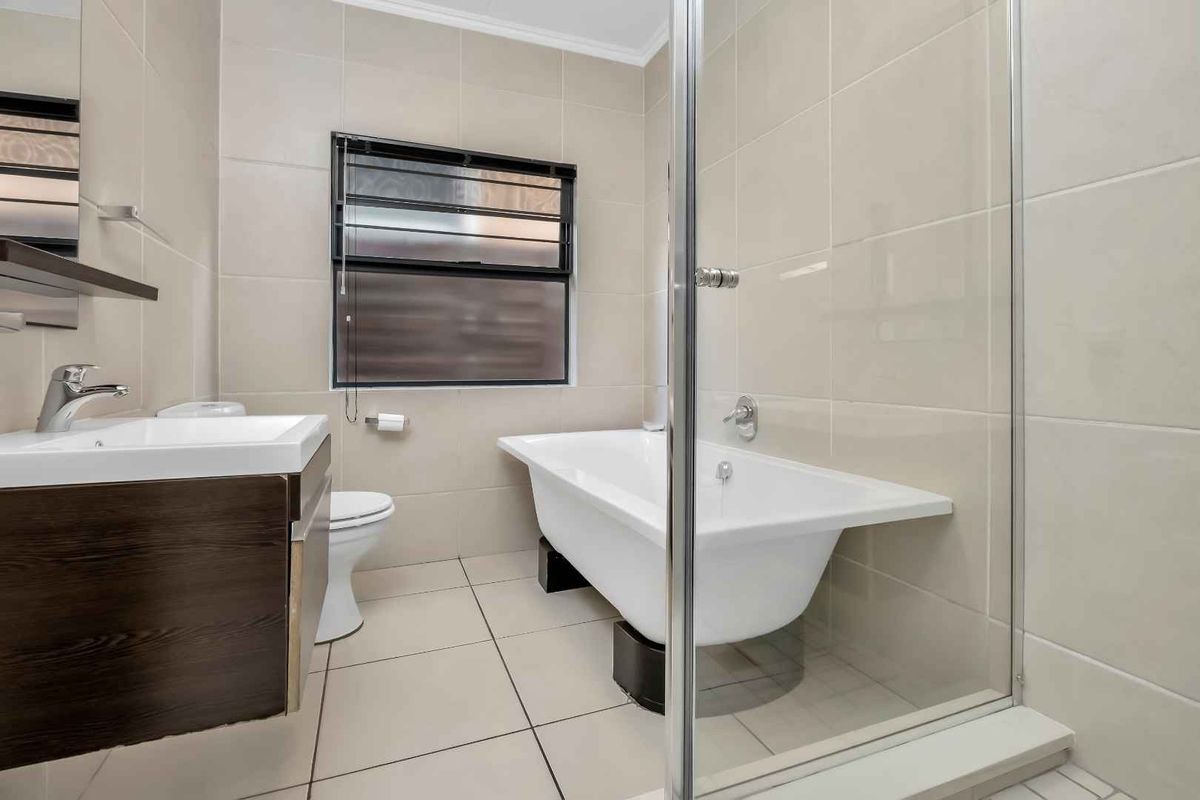 Modern bathroom featuring a freestanding bathtub, glass-enclosed shower, wall-mounted vanity with basin, and neutral floor-to-ceiling tiling.