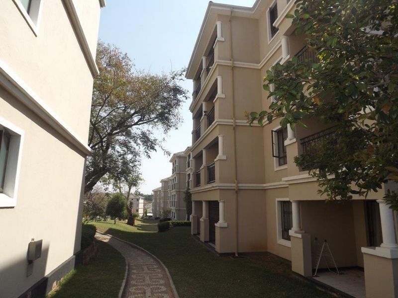 Exterior view of the apartment complex featuring multi-story residential blocks, private balconies, and a well-maintained paved garden walkway.