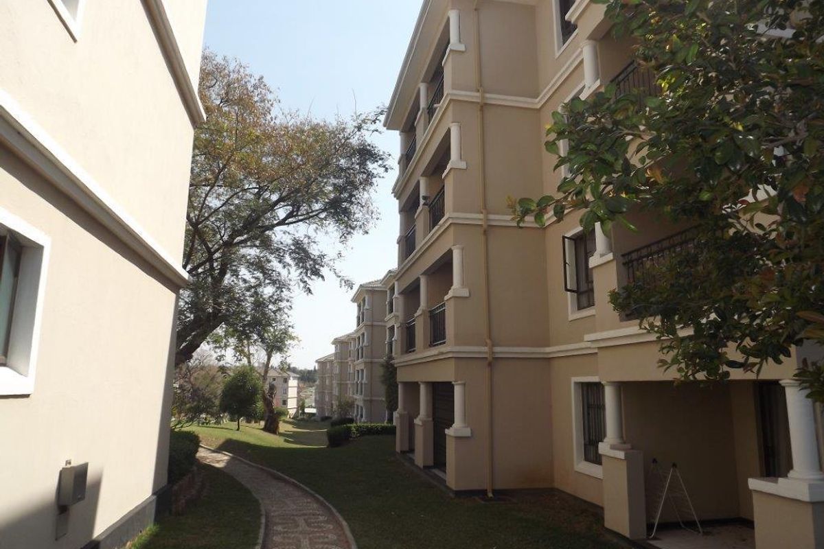 Exterior view of the apartment complex featuring multi-story residential blocks, private balconies, and a well-maintained paved garden walkway.