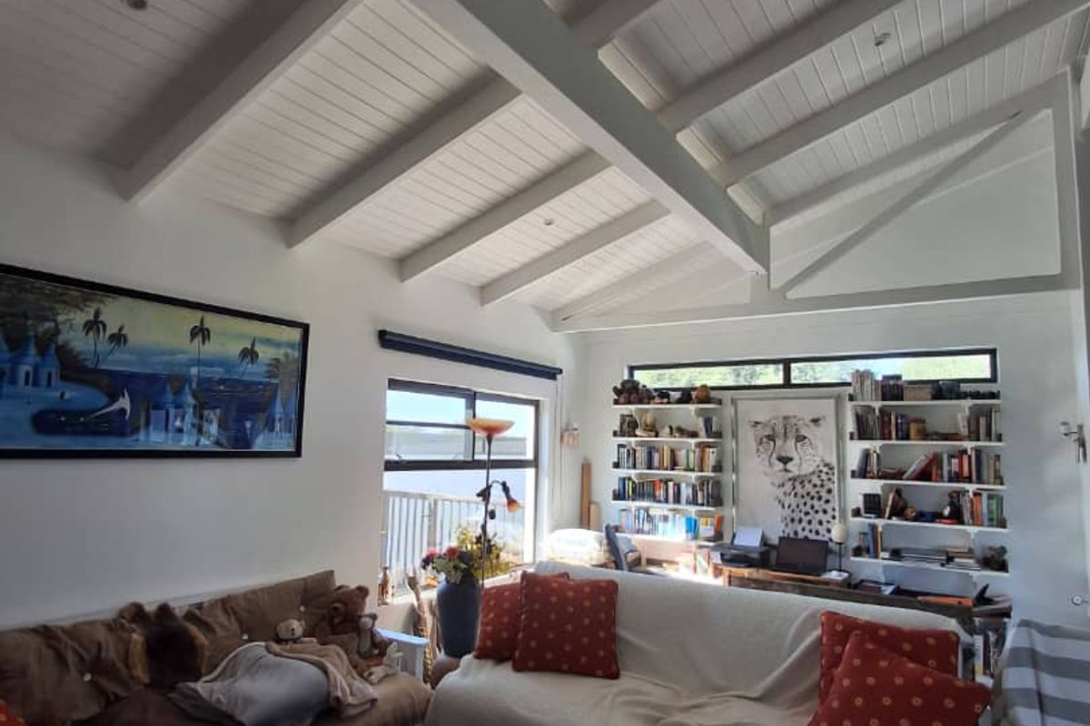 Spacious living room featuring a high vaulted ceiling with exposed timber beams, large windows for natural light, and integrated built-in shelving units.