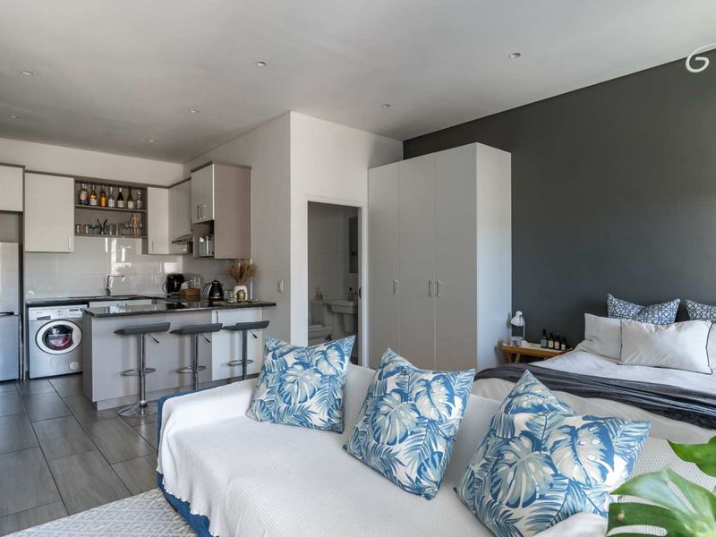 An open-plan studio apartment featuring a modern kitchen with built-in cabinetry, integrated laundry, and a bedroom area with built-in wardrobes.