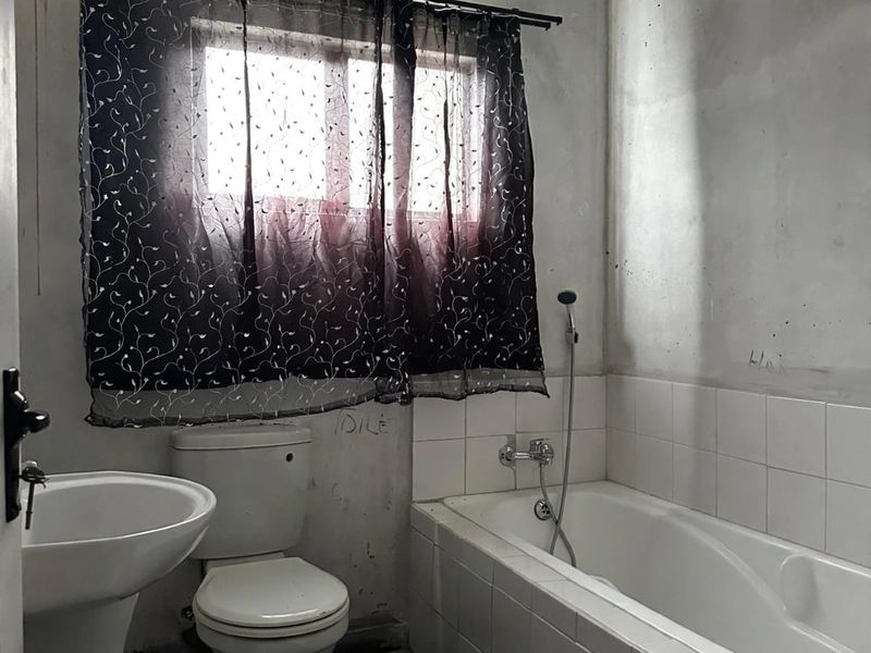 A bathroom featuring a pedestal basin, toilet, and built-in bathtub with shower mixer, currently requiring wall finishing and cosmetic updates.