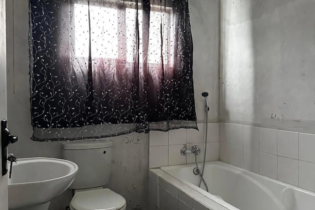 A bathroom featuring a pedestal basin, toilet, and built-in bathtub with shower mixer, currently requiring wall finishing and cosmetic updates.