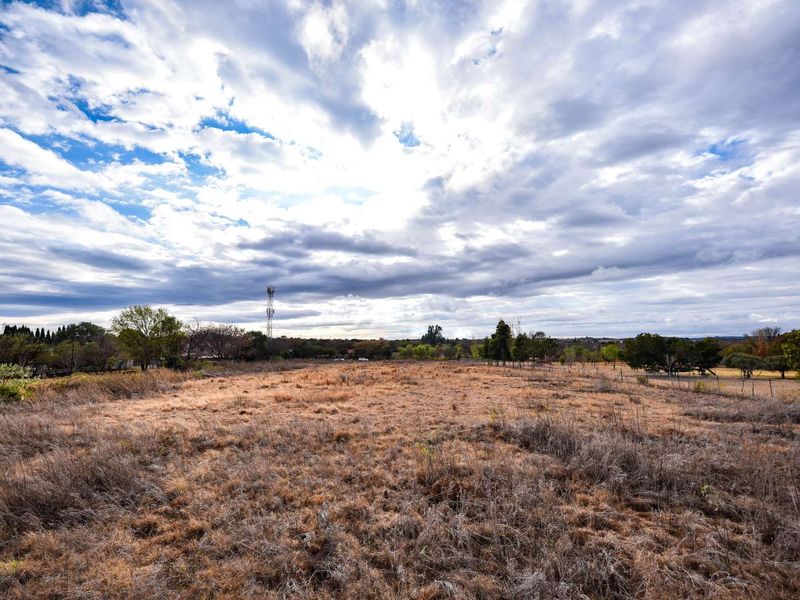 A wide-angle view of a vacant residential plot featuring dry grass and perimeter wire fencing under a cloudy sky.
