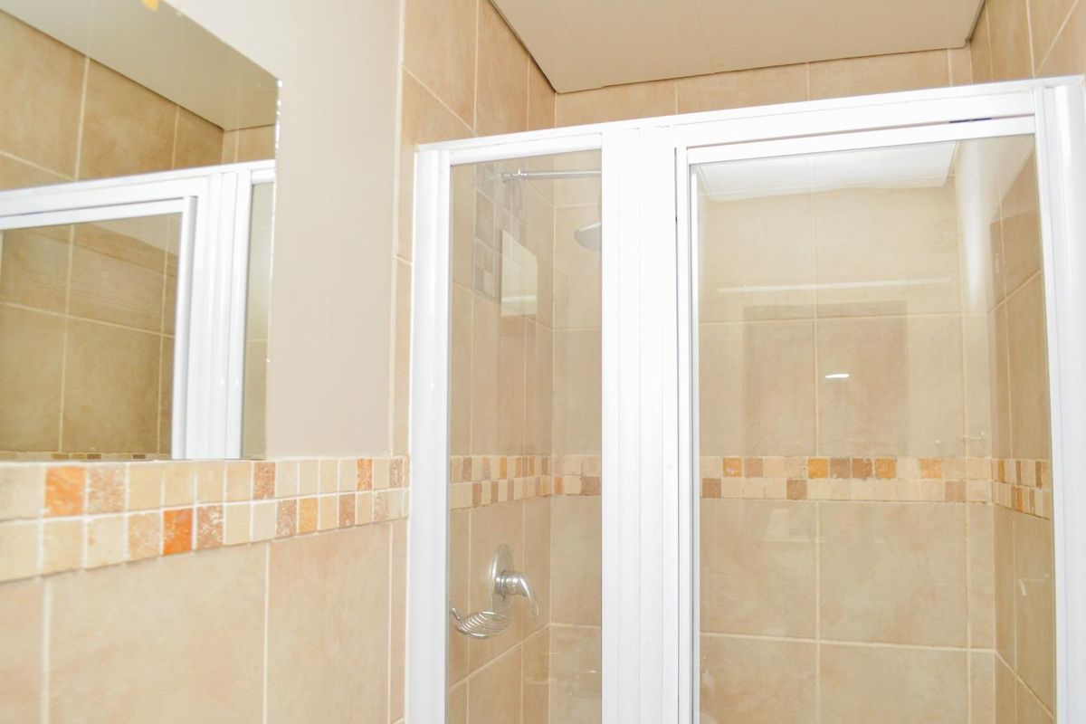 A functional bathroom featuring a glass-enclosed shower with neutral wall tiling and a wall-mounted mirror.