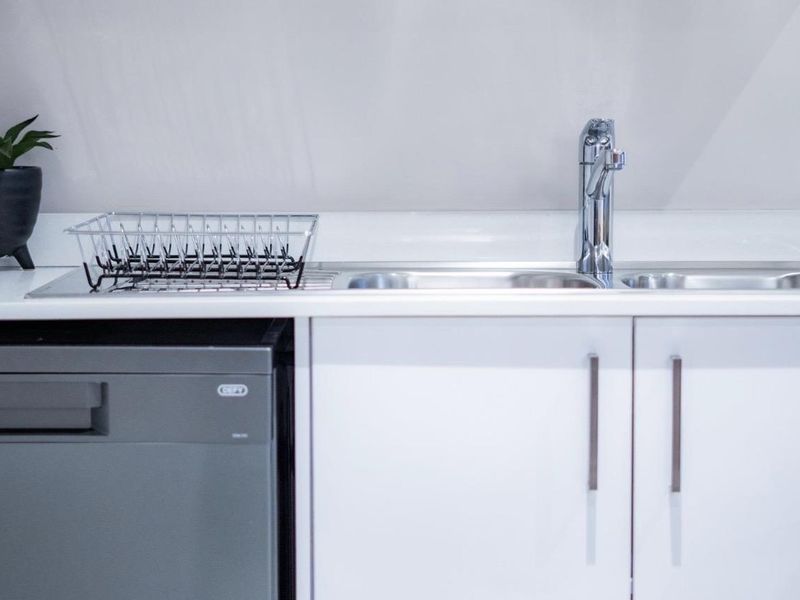 A clean and modern kitchen area featuring white cabinetry, a stainless steel sink with a chrome mixer tap, and an integrated dishwasher.