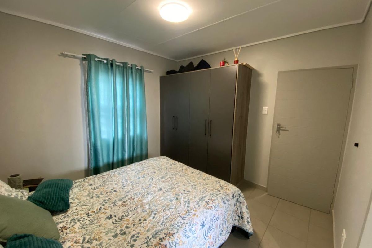 A functional bedroom featuring tiled flooring, a built-in wardrobe, and a standard door, providing a clean and practical living space.