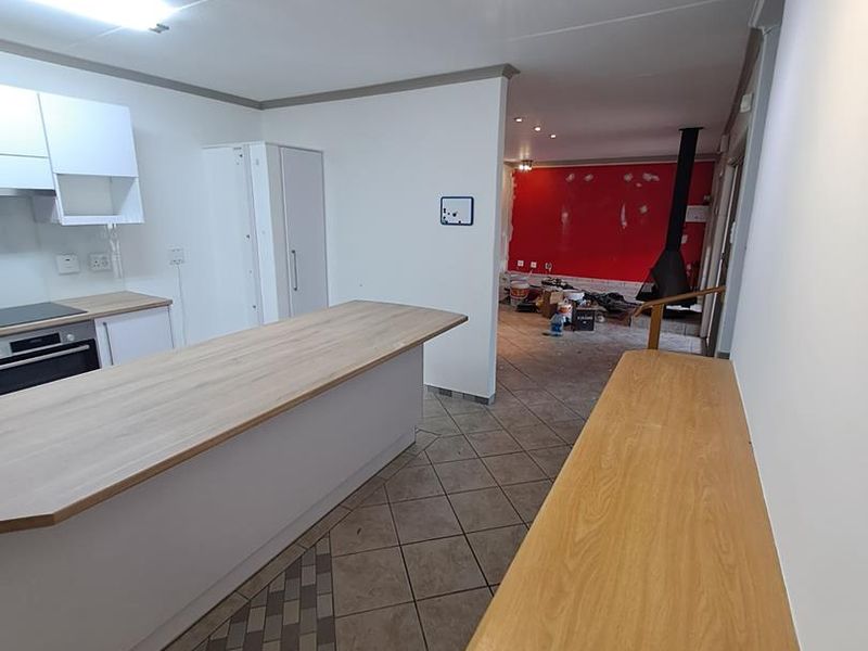 Open-plan kitchen and living area featuring a central island, built-in appliances, and a fireplace, currently undergoing renovation with unfinished wall surfaces.