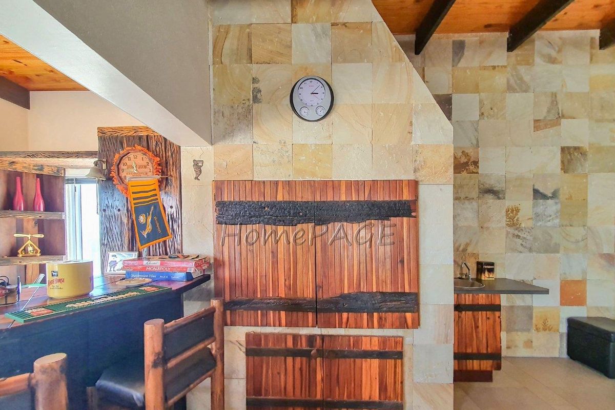 A rustic indoor entertainment area featuring a stone-clad fireplace, built-in wooden cabinetry, and a bar counter with exposed timber ceiling beams.