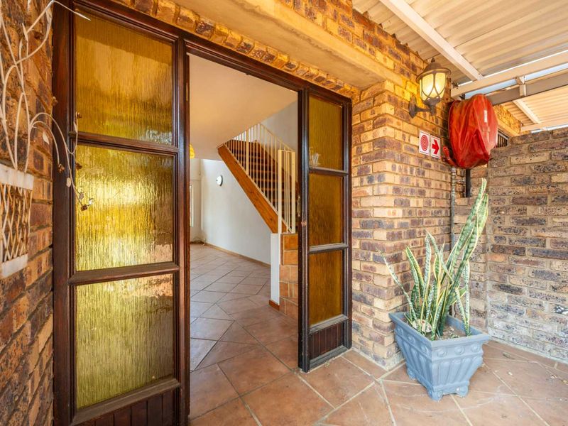 Entrance area featuring face brick walls, tiled flooring, and a timber-framed glass door leading into the home with an internal staircase visible.