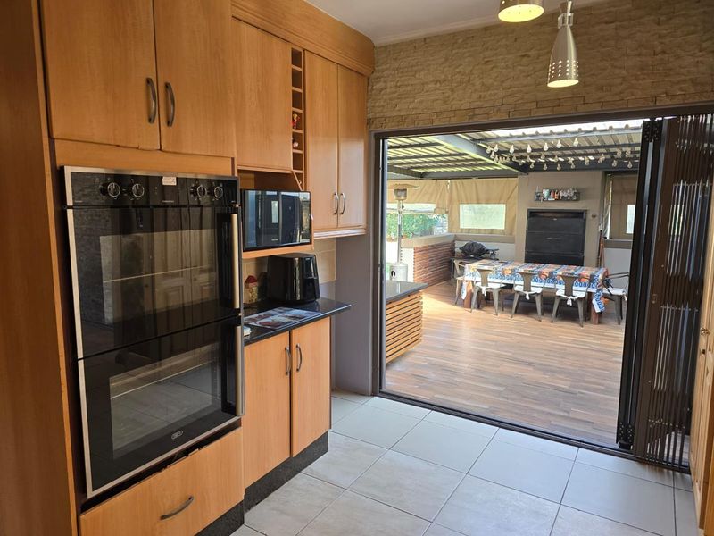 A functional kitchen featuring built-in double ovens and laminate cabinetry, with seamless access through stacking doors to an outdoor patio entertainment area.