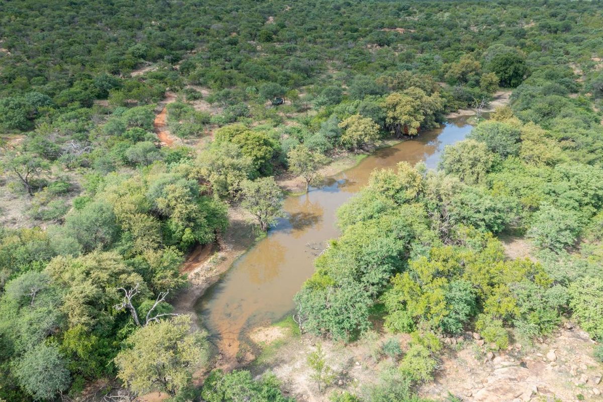 An aerial view of a natural water dam surrounded by lush indigenous bushveld vegetation and trees.