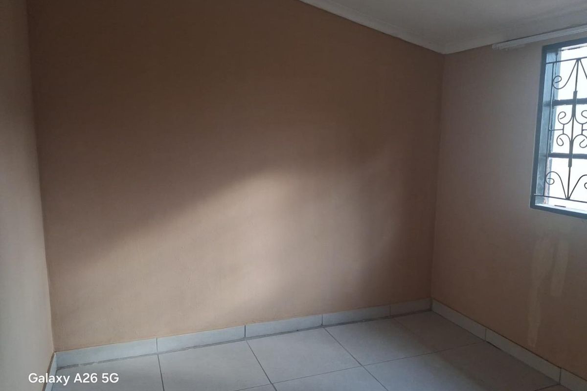 An empty bedroom featuring tiled flooring and a window with security bars, presenting a blank canvas for potential interior design updates.
