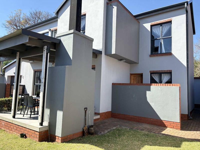 Rear view of the townhouse featuring a covered patio, brick paved area, and a low brick boundary wall with a well-maintained exterior facade.