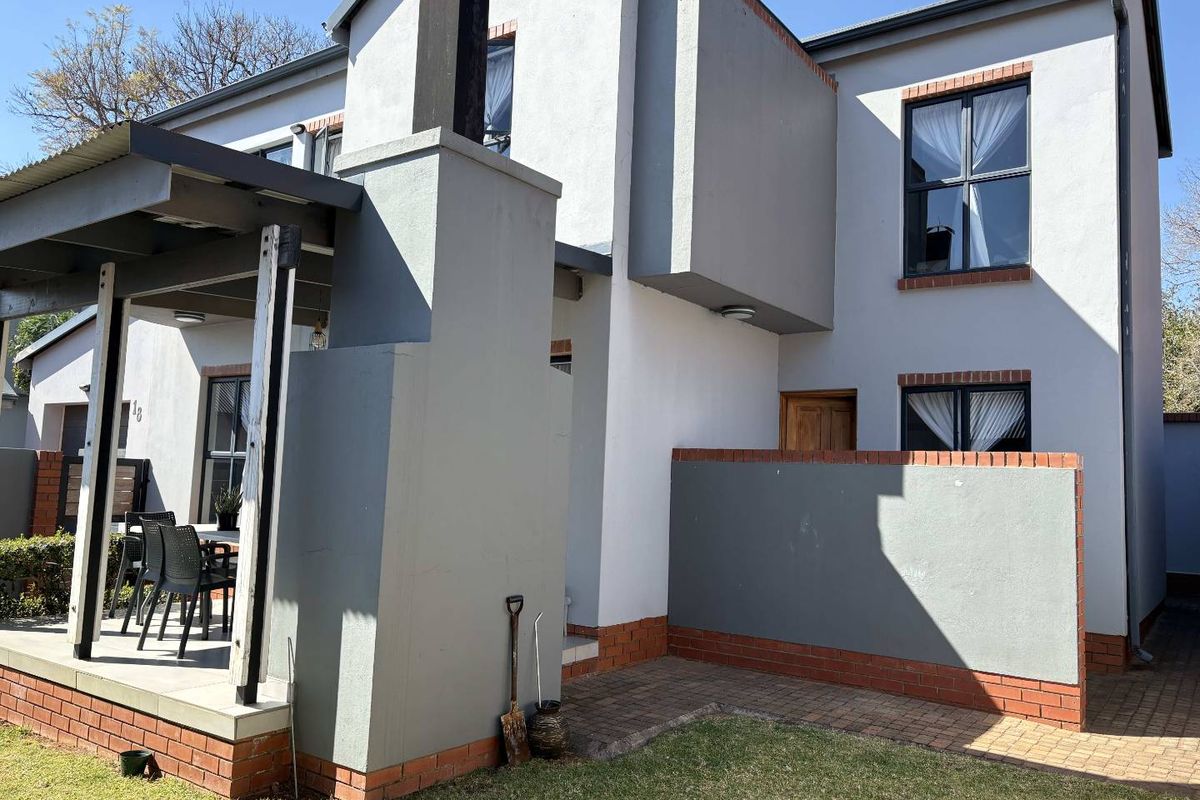 Rear view of the townhouse featuring a covered patio, brick paved area, and a low brick boundary wall with a well-maintained exterior facade.