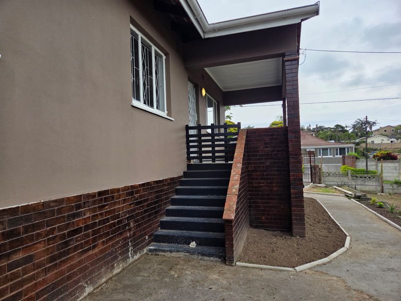 Exterior view of the front entrance featuring a covered porch, brick staircase, and concrete walkway leading to the main door.