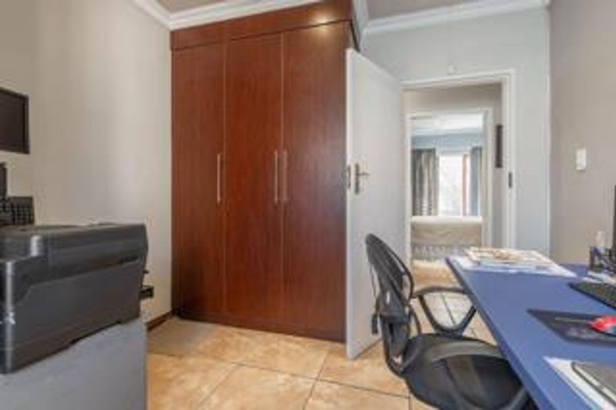 A bedroom featuring built-in wooden cupboards, tiled flooring, and decorative cornicing, with a view into an adjacent room.