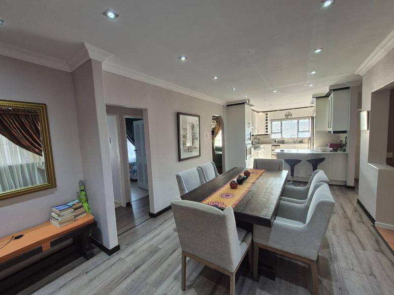 Open-plan dining area featuring modern laminate flooring, recessed lighting, and a seamless transition into a functional kitchen with built-in cabinetry and island.