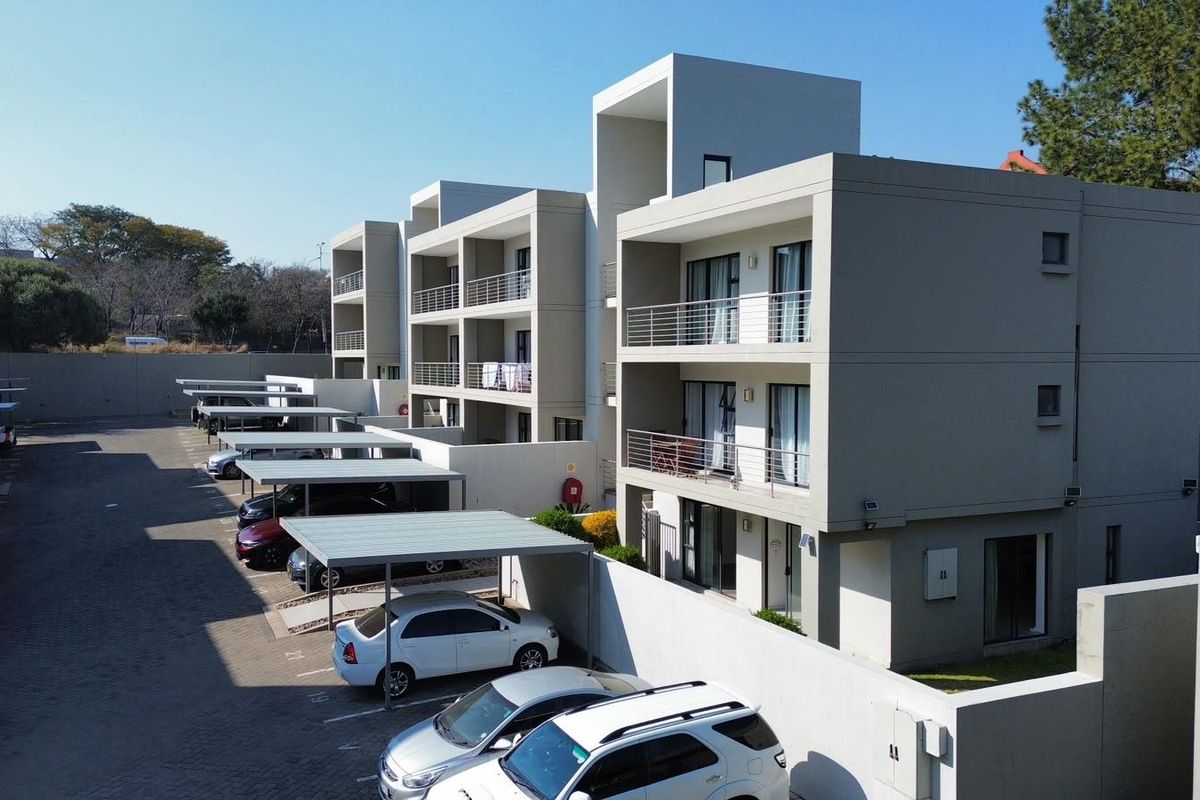Aerial view of a modern apartment complex featuring multi-level balconies and dedicated covered parking bays within a secure paved area.