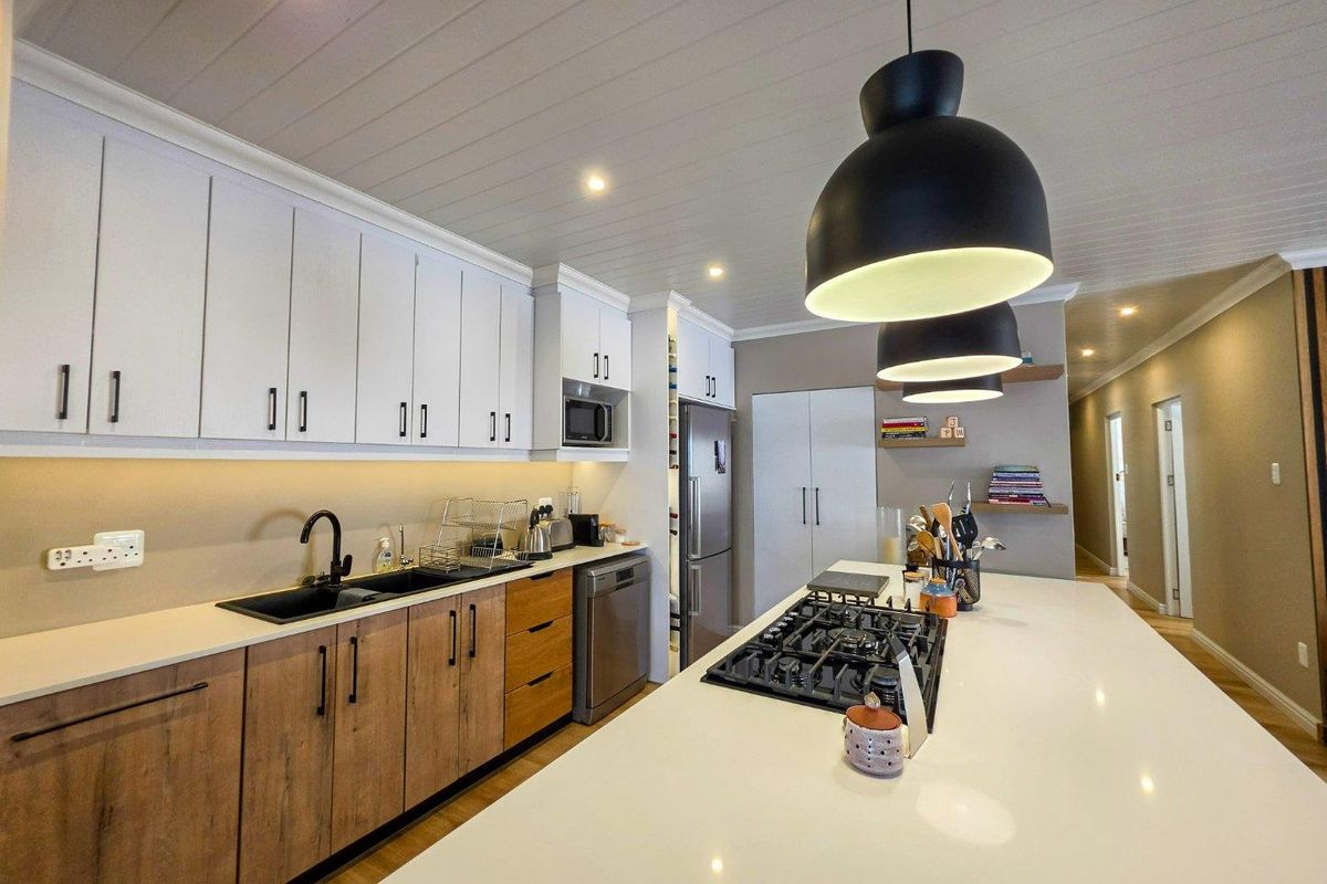 Modern kitchen featuring a large island with a gas hob, quartz countertops, two-tone cabinetry, and integrated appliances under a stylish tongue and groove ceiling.