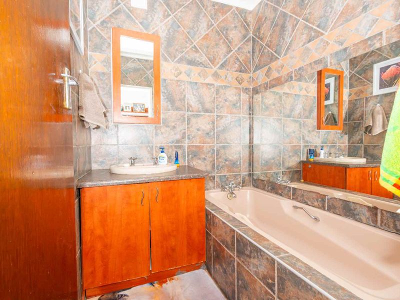A dated bathroom featuring a built-in vanity, drop-in basin, and bathtub with full-height wall tiling.