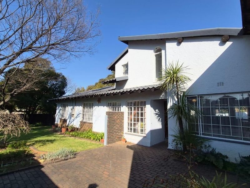 A rear view of the house featuring a brick paved patio area, established garden, and traditional steel frame windows under a tiled roof.