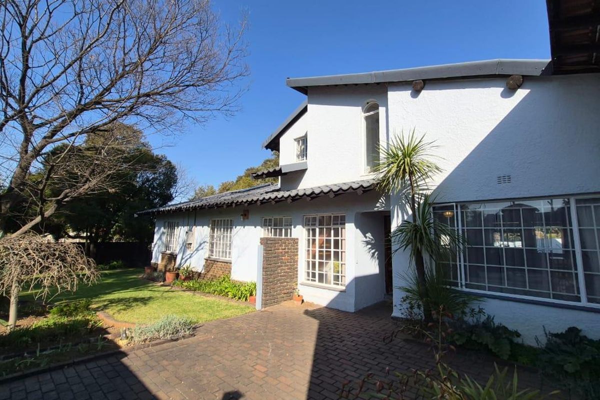 A rear view of the house featuring a brick paved patio area, established garden, and traditional steel frame windows under a tiled roof.