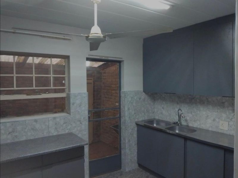 A functional kitchen featuring dark built-in cabinetry, double stainless steel sink, and tiled splashbacks, offering a clean space ready for modernization.