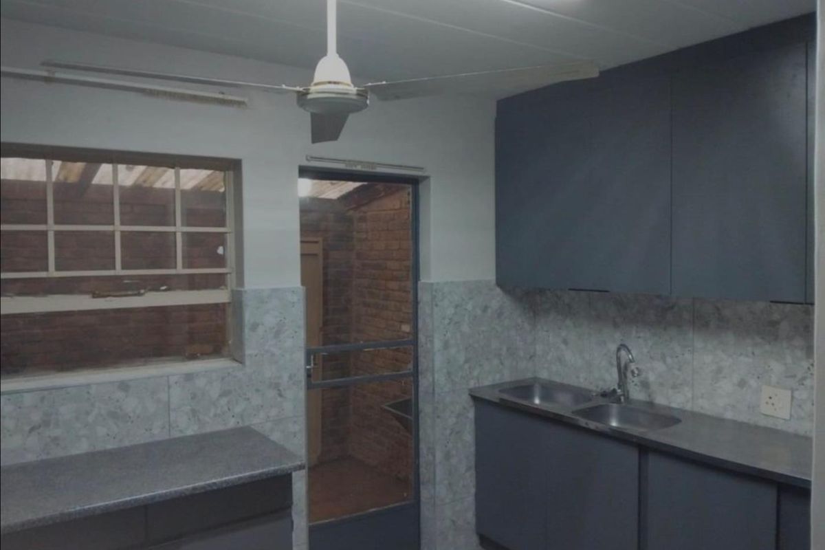 A functional kitchen featuring dark built-in cabinetry, double stainless steel sink, and tiled splashbacks, offering a clean space ready for modernization.